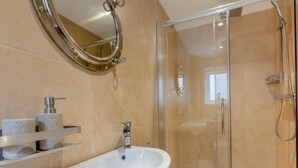 Ein Badezimmer mit einem weißen Waschbecken, einer Duschkabine aus Glas und einem Spiegel mit dekorativem Rahmen.