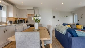 Eine moderne Küche mit weißen Schränken, einem Esstisch mit Stühlen und einem blauen Sofa im Wohnbereich.