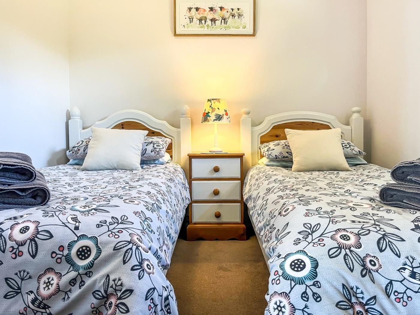 Een hotelkamer met twee bedden, een nachtkastje met een lamp en een ingelijst schilderij aan de muur.