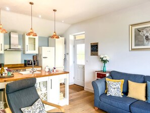 A modern kitchen with white cabinets, a microwave, and a coffee machine. There is a blue sofa with patterned cushions in the living area.
