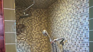 Une douche équipée d’un pommeau de douche à main et d’un robinet mural, dont les parois sont recouvertes de carreaux formant une mosaïque.