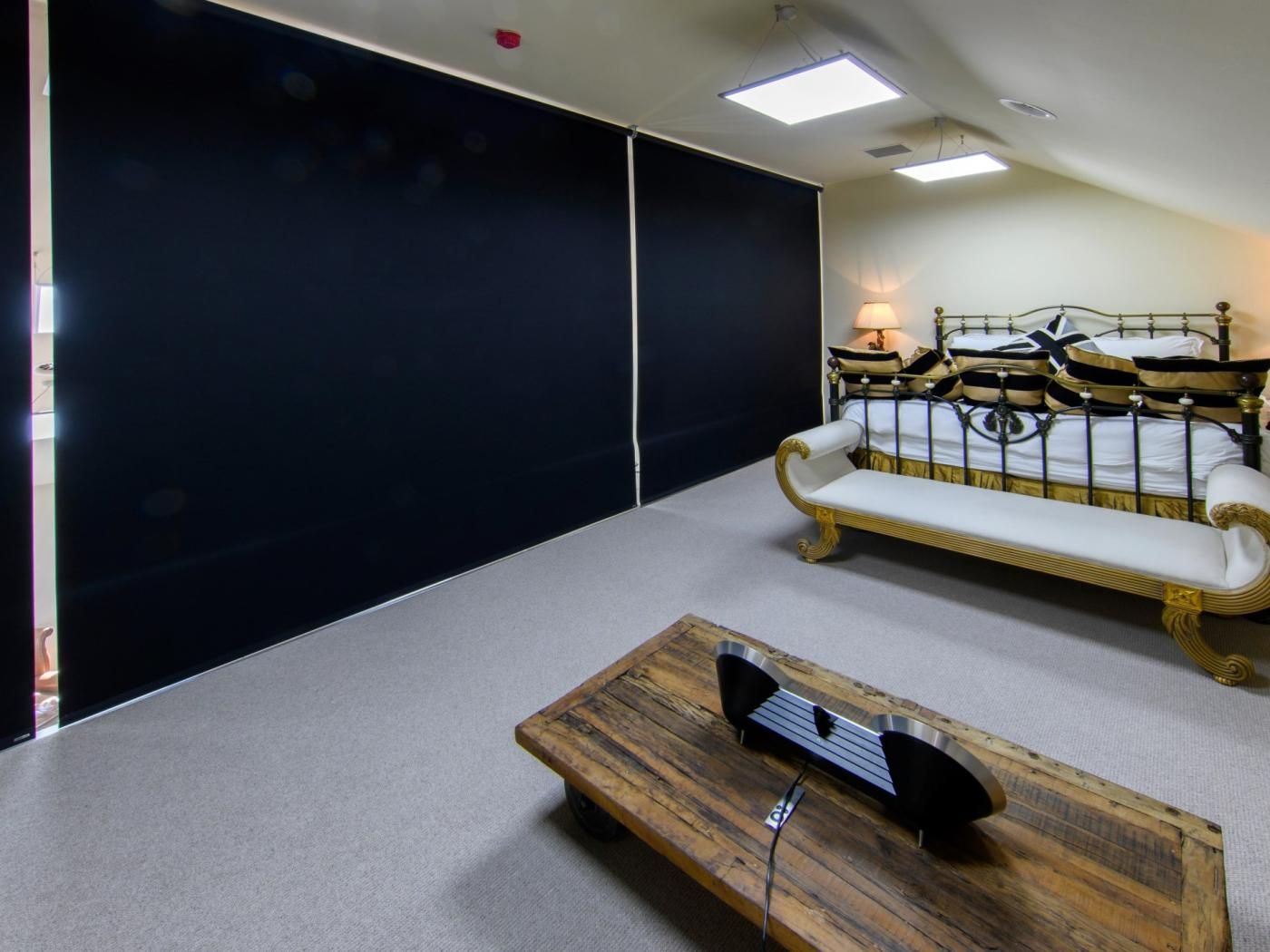 A hotel room with a large bed, a bench, a wooden table, and a black screen wall.