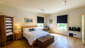 Una camera da letto con pavimento in legno, un letto con biancheria bianca, un comò, un comodino con una lampada, una sedia con un cuscino di Topolino e una finestra con tende oscuranti.