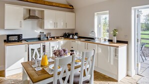 Eine Küche mit weißen Schränken, einer Holz Arbeitsplatte, einer eingebauten Mikrowelle und einem Essbereich mit weißen Stühlen und einem für das Frühstück gedeckten Tisch.