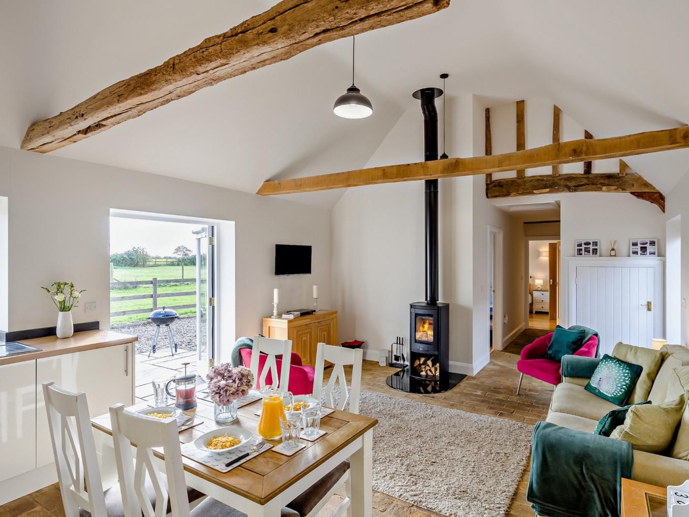 A spacious living area with a fireplace, wooden beams, a dining table with breakfast, and a view to the outside.