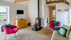 Ein gemütliches Wohnzimmer mit Kamin, Holzbalken, einem Fernseher und einer Couch mit Kissen.