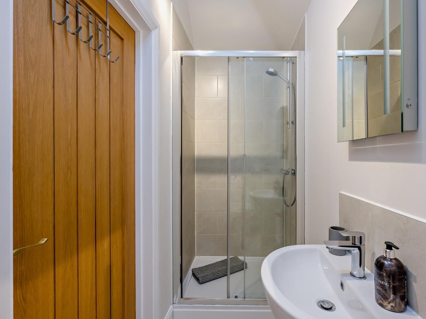 Un bany modern amb dutxa de vidre, un armari de fusta, un lavabo blanc i un mirall.