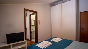 Ein Schlafzimmer mit Bett, Fernseher auf einem Schrank, Kleiderschrank und einem durch eine offene Tür einsehbaren Badezimmer.
