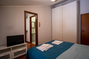 A bedroom with a bed, a TV on a stand, a wardrobe, and a bathroom visible through an open door. - A comfortable 65 sqm apartment, suitable for up to 3 people, located on the first floor of a building without an elevator (access via stairs).The property is strategically located just 50 meters from the hospital.Piacenza city center is easily accessible (Piacenza)