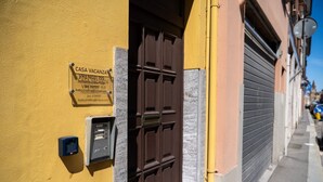 Ein gelbes Gebäude mit geschlossenem Rollo, einer braunen Tür und einem Schild mit der Aufschrift 'CASA VACANZA VIRENOZI 155'.