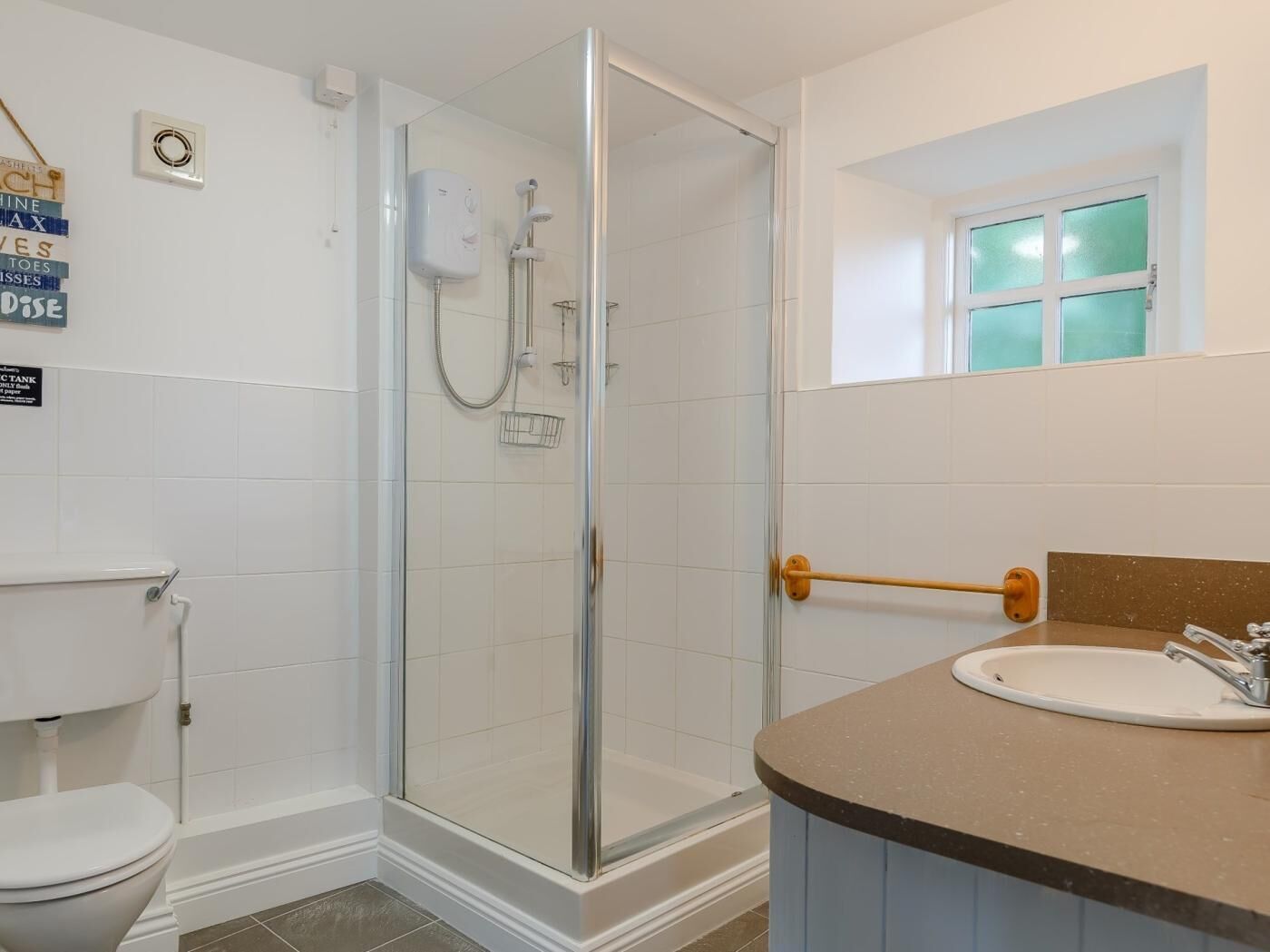 A bathroom with a glass-enclosed shower, a white toilet, and a sink with a towel rack.