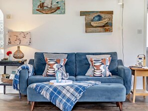 Un salon moderne avec un canapé bleu, des coussins décoratifs, une table basse et des œuvres d’art murales.