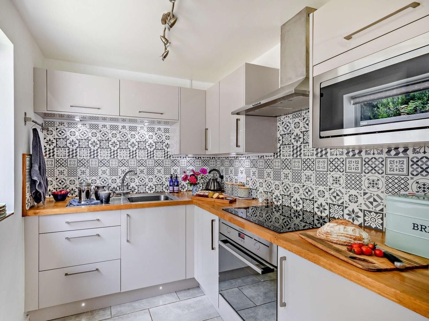 A kitchen with white cabinets, patterned backsplash, stainless steel appliances, and a wooden countertop.