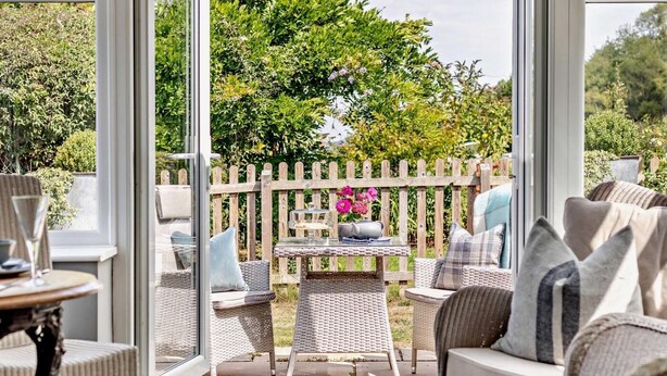 En patio med fletningsmøbler, et bord med en blomstervase og et træhegn.