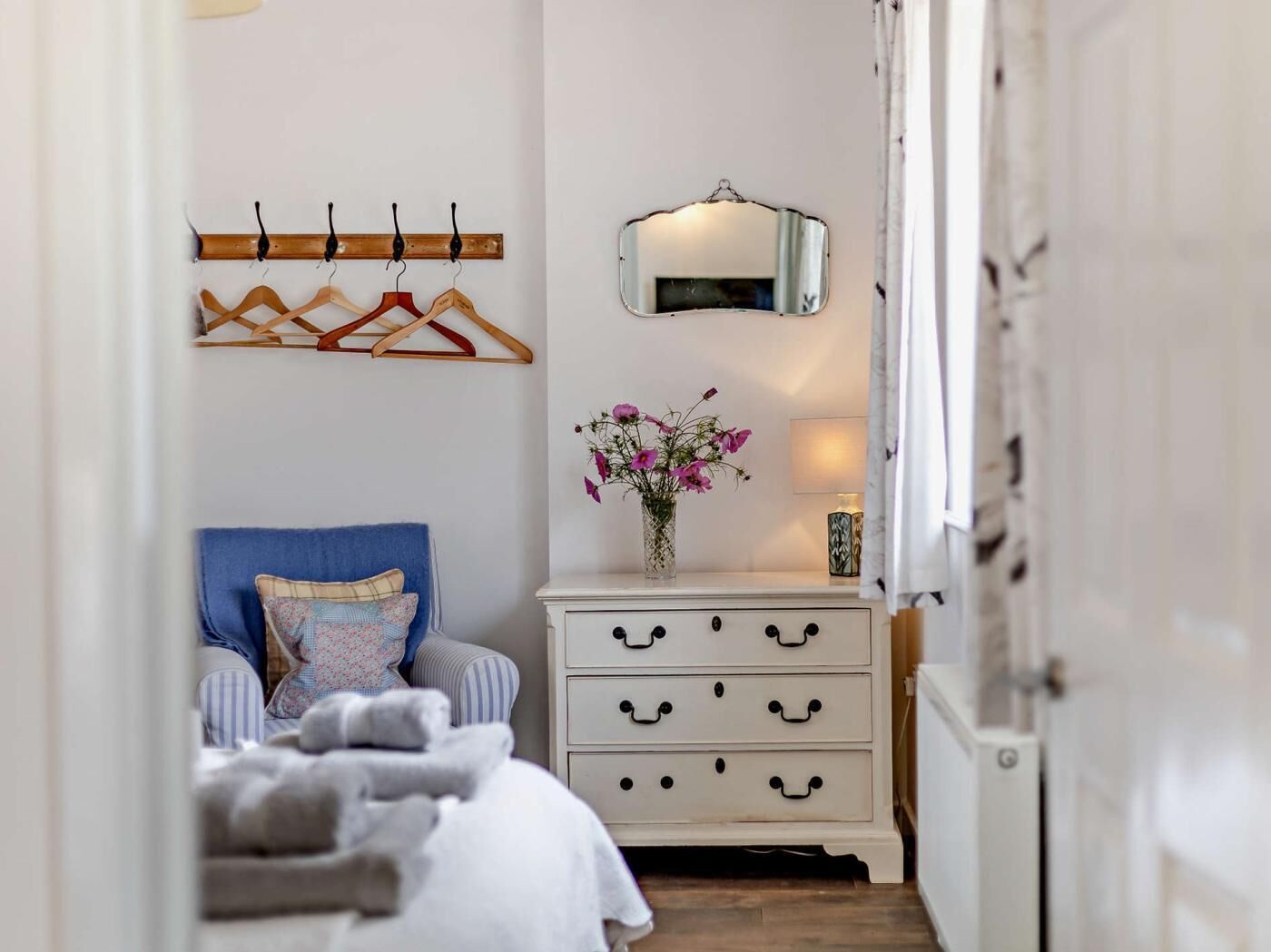 Un dormitorio con cama, cómoda con cajones, espejo y perchero con ganchos.