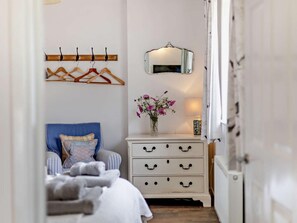 Une chambre à coucher comprenant un lit, une commode avec des tiroirs, un miroir et un porte-manteau avec des cintres.