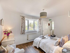 Une chambre à coucher comprenant un lit, une table de chevet, une chaise, une fenêtre avec des rideaux, un radiateur et une porte.