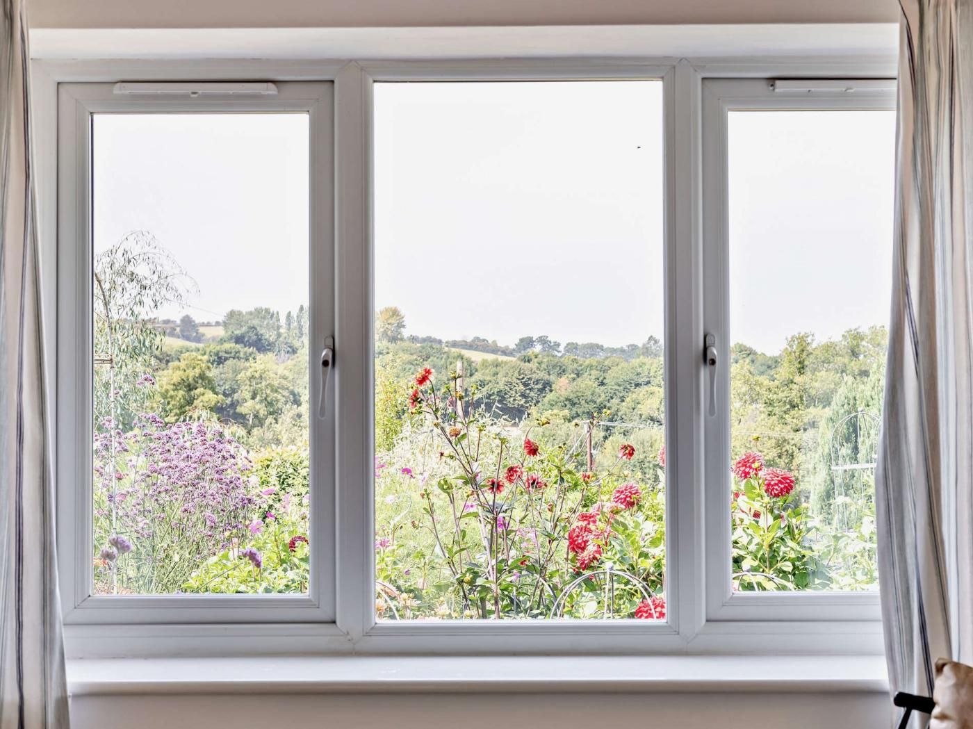 A room with a large window overlooking a garden with various plants and flowers.