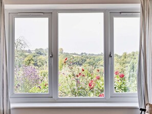 Une pièce dotée d’une grande fenêtre donnant sur un jardin où poussent différentes plantes et fleurs.