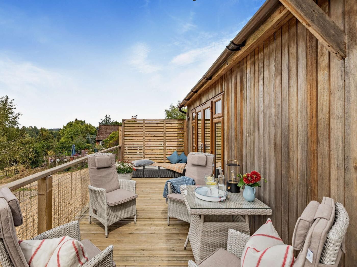 Une terrasse en bois avec des meubles en osier, une table avec des boissons et une vue sur la campagne.