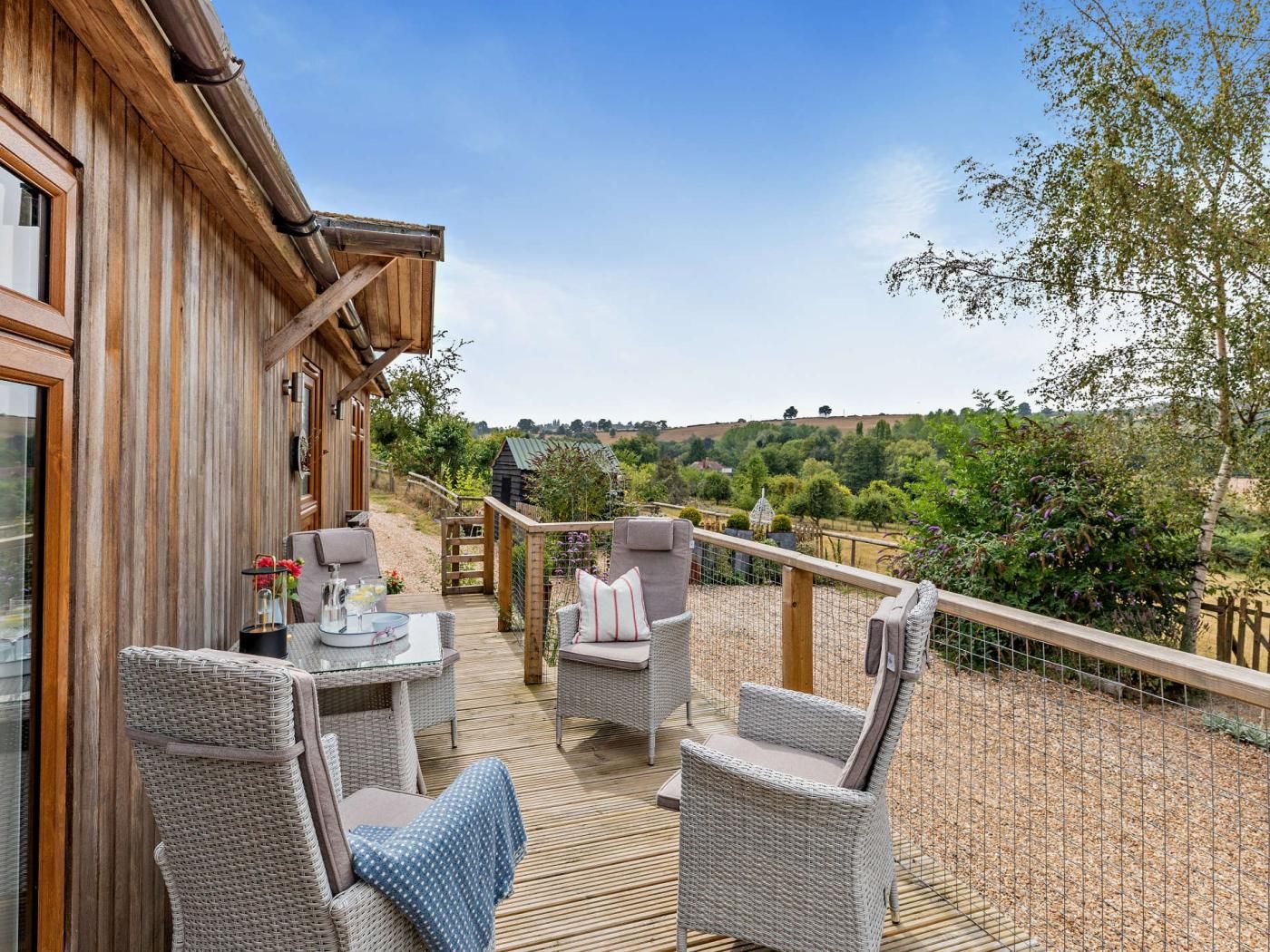 A wooden deck with wicker furniture, a table with a drink, and a view of a rural landscape.
