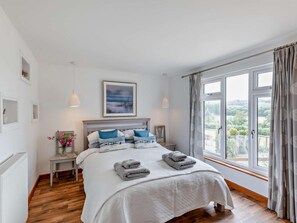 A bedroom with a large bed, a view of the outdoors, and a window with curtains.