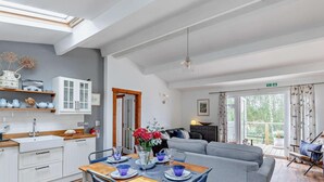 Eine moderne Küche mit weißen Schränken, einem Esstisch für vier Personen und einem grauen Sofa im Wohnbereich.