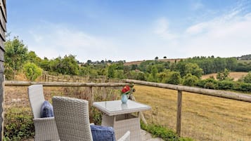 A patio with wicker furniture and a table, overlooking a rural landscape with fields and trees.