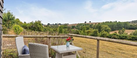 A patio with wicker furniture and a table, overlooking a rural landscape with fields and trees.