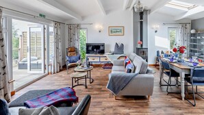 Ein geräumiges Wohnzimmer mit Fernseher, Sofa, Esstisch und Kamin.