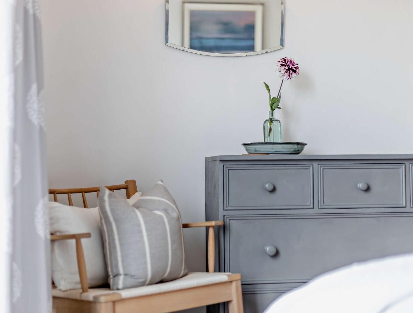 A bedroom with a wooden bed, a grey dresser, and a small vase with a flower on top.