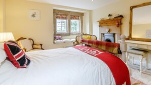 Ein Schlafzimmer mit einem Bett, einem Schreibtisch, einem Stuhl, einer Kommode, einem Spiegel und einem Fenster mit Vorhängen.