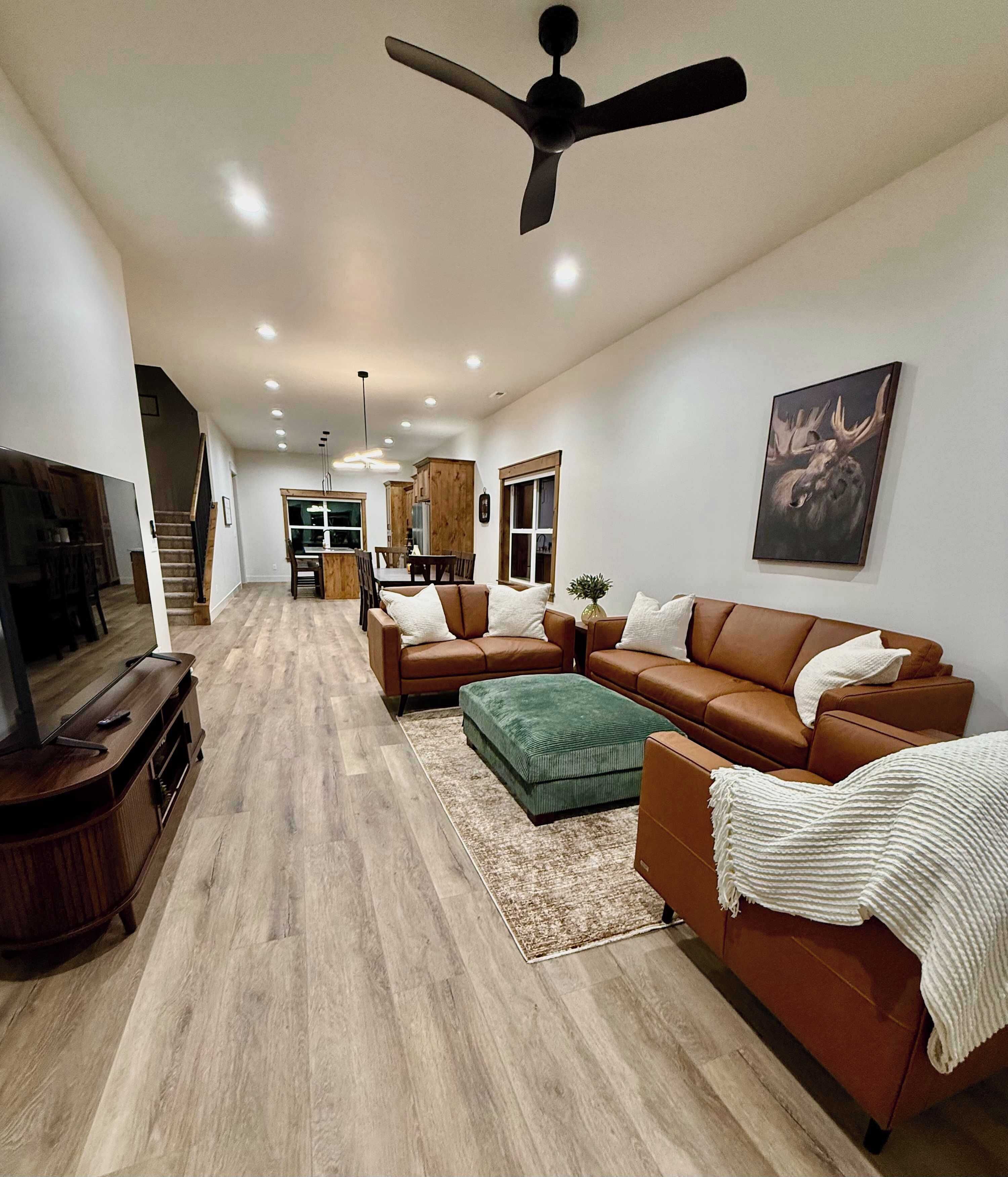 A spacious living area with a brown leather sofa, a green ottoman, and a television on a wooden stand.