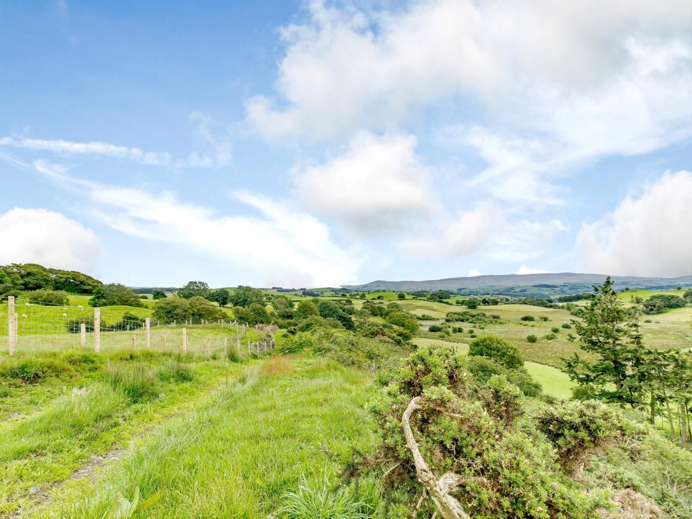 Un paysage rural caractérisé par des collines douces, une zone délimitée par une clôture et un ciel dégagé.
