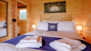 A wooden cabin room with a bed, a painting on the wall, and a window. - 1 Bed in Torpoint (oc-78680) (Deviock)