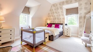 Une chambre à coucher avec un lit, un berceau, une commode, une chaise et une fenêtre.
