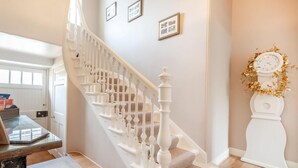 Un escalier avec des balustrades blanches, une horloge ornée de motifs dorés et des tableaux encadrés accrochés au mur.