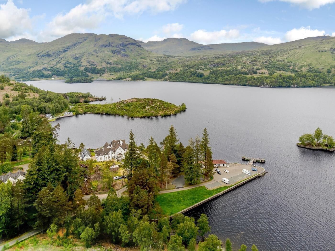 Un lac entouré de collines, une jetée où sont garées des voitures et un bâtiment doté de nombreuses fenêtres.