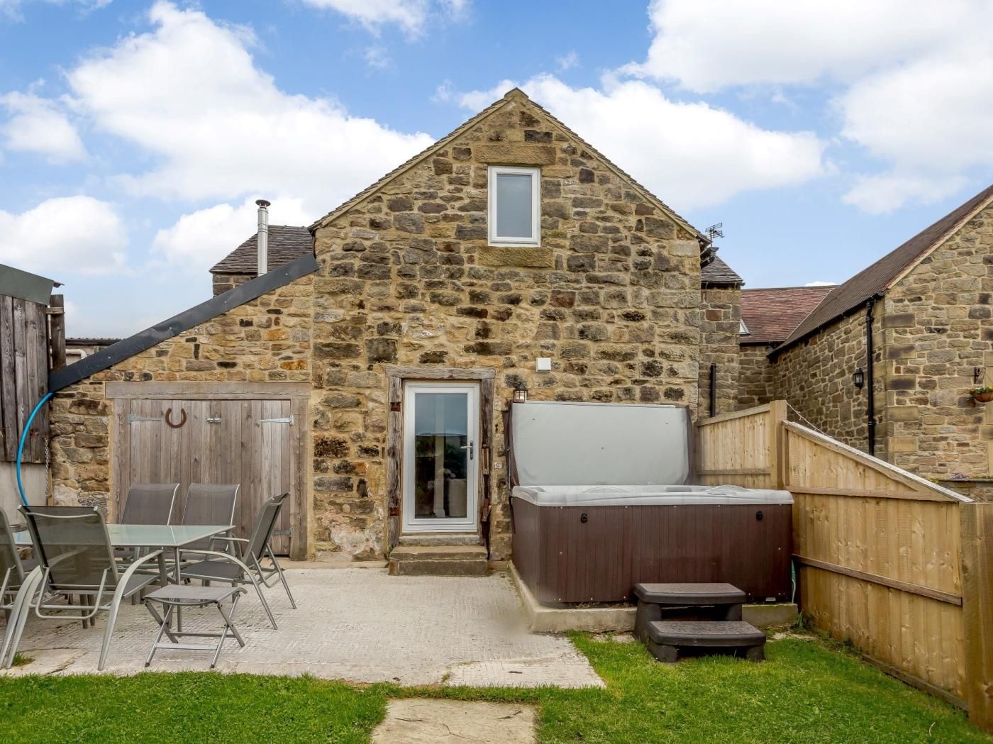 A stone building with a wooden door, a hot tub, and a patio with chairs and tables.