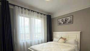 A bedroom with a bed, a window with curtains, a ceiling light, a wall-mounted picture, and a marble-patterned rug. - Beautiful and well furnished one bedroom apartment in a well secured area. (Nairobi)
