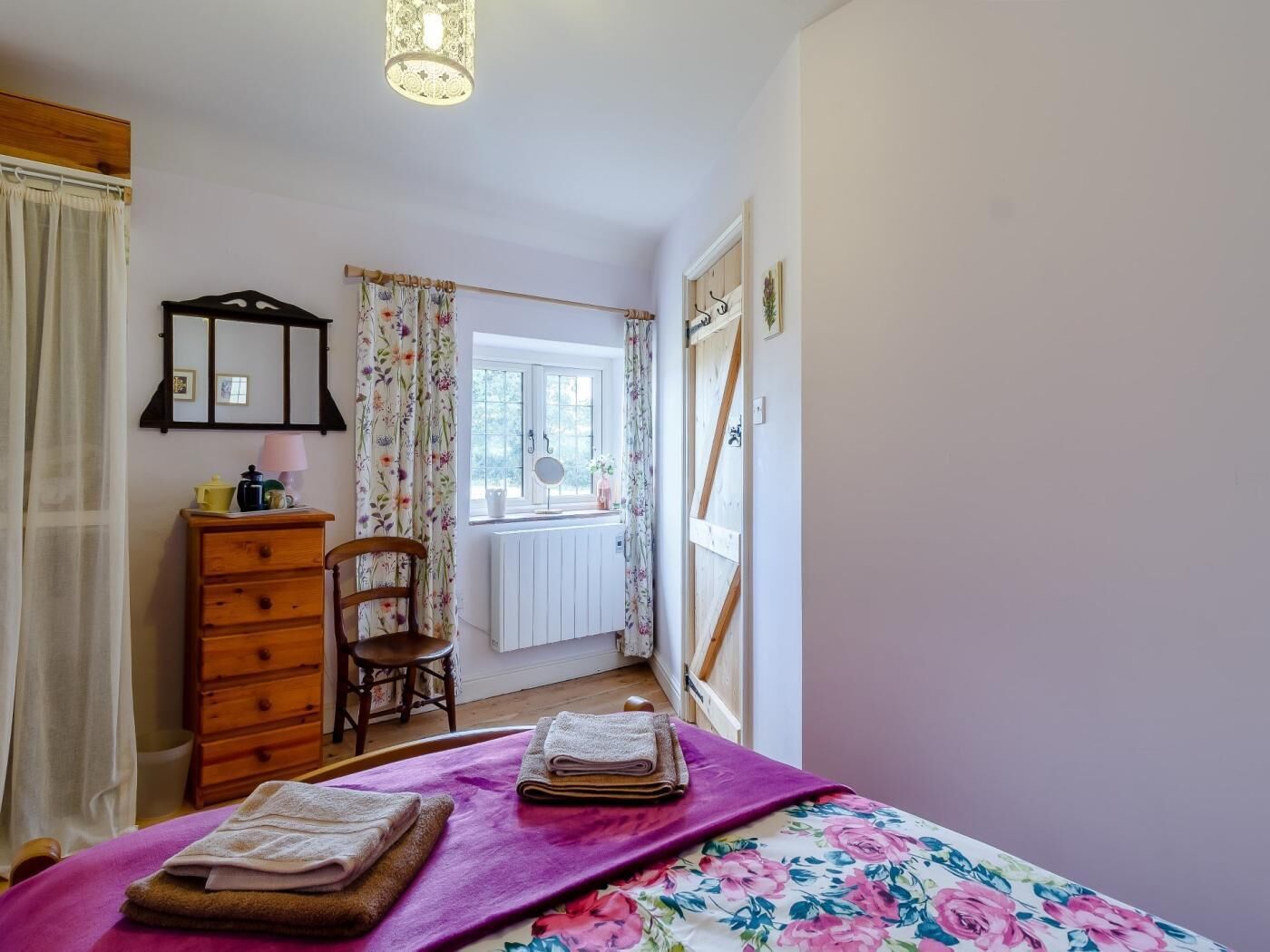 Ein Schlafzimmer mit Bett, Kommode, Sessel, einem Fenster mit Vorhängen und einer Heizung.