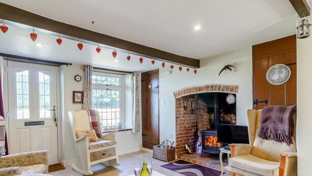 A cozy living room with a fireplace, floral-patterned furniture, and a table with a bottle and glasses. - 3 Bed in North Walsham (oc-78708) (Honing)