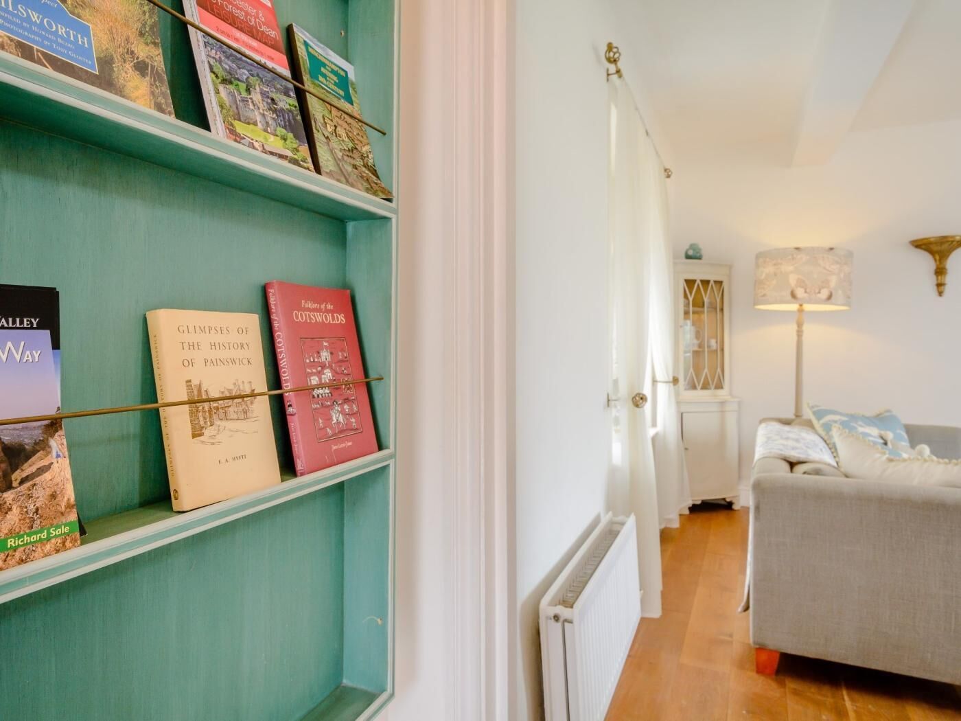 A hallway with teal shelves holding books, a white radiator, a grey sofa, and a lamp.