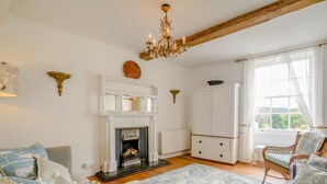 Una sala de estar con chimenea, una araña, un mueble blanco y vistas al exterior por una ventana.