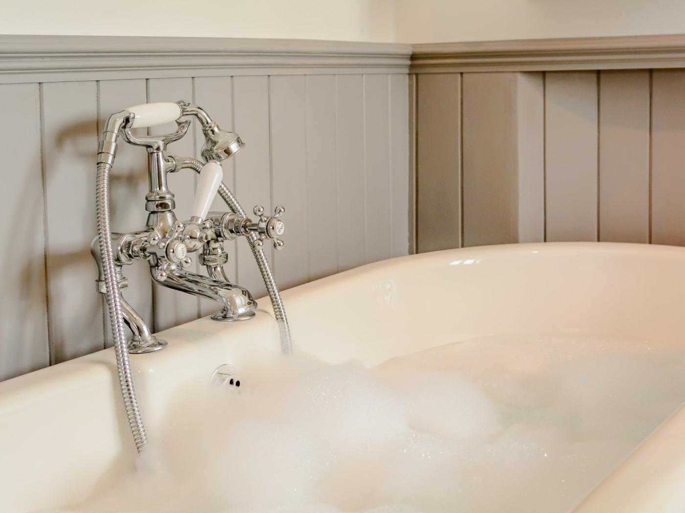 Une baignoire équipée d’un pommeau de douche et d’un tuyau, un lavabo blanc et un mur recouvert de panneaux en bois.
