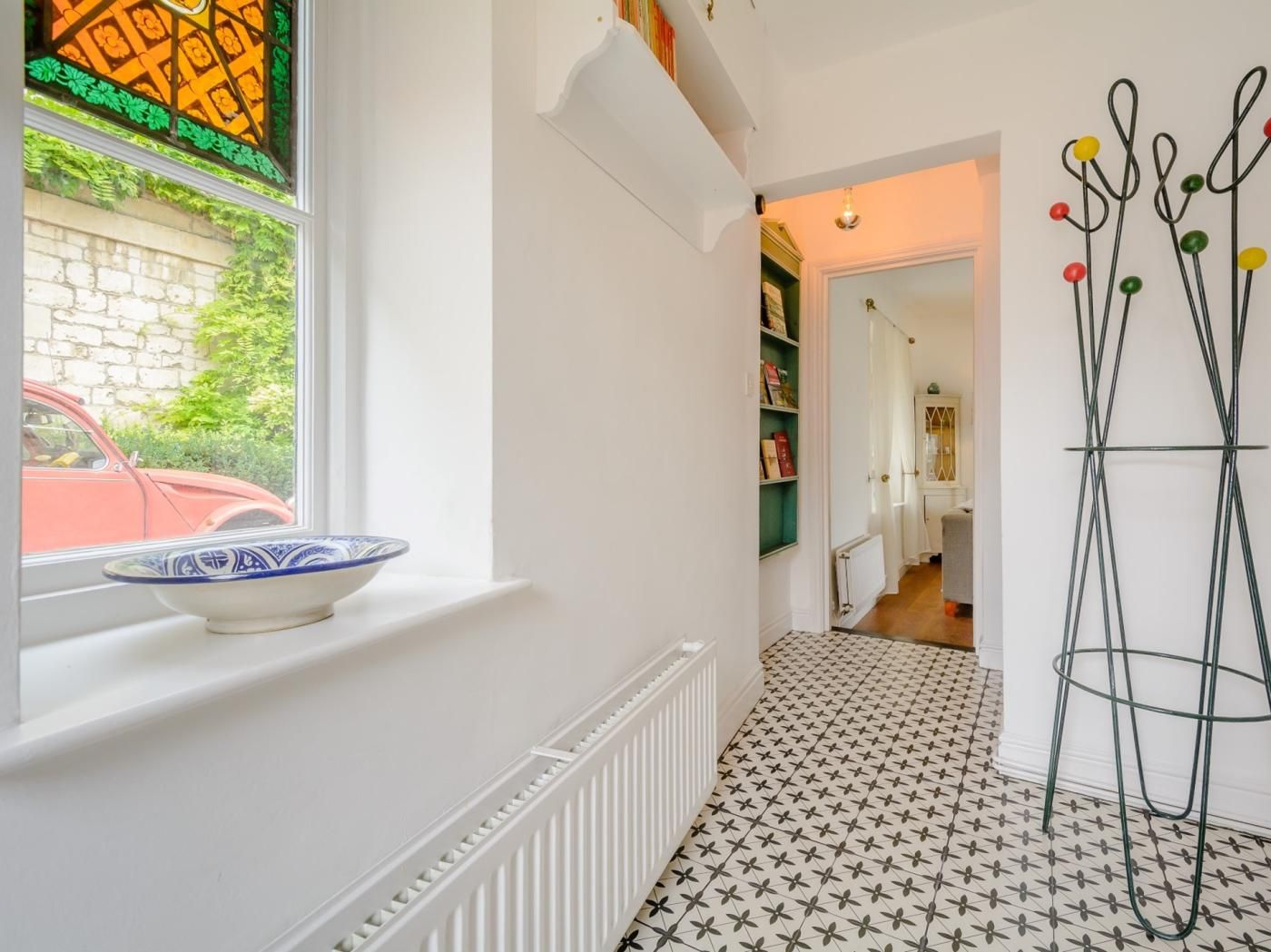 A hallway with a radiator, a bowl on the windowsill, a patterned floor, and a door leading to another room.
