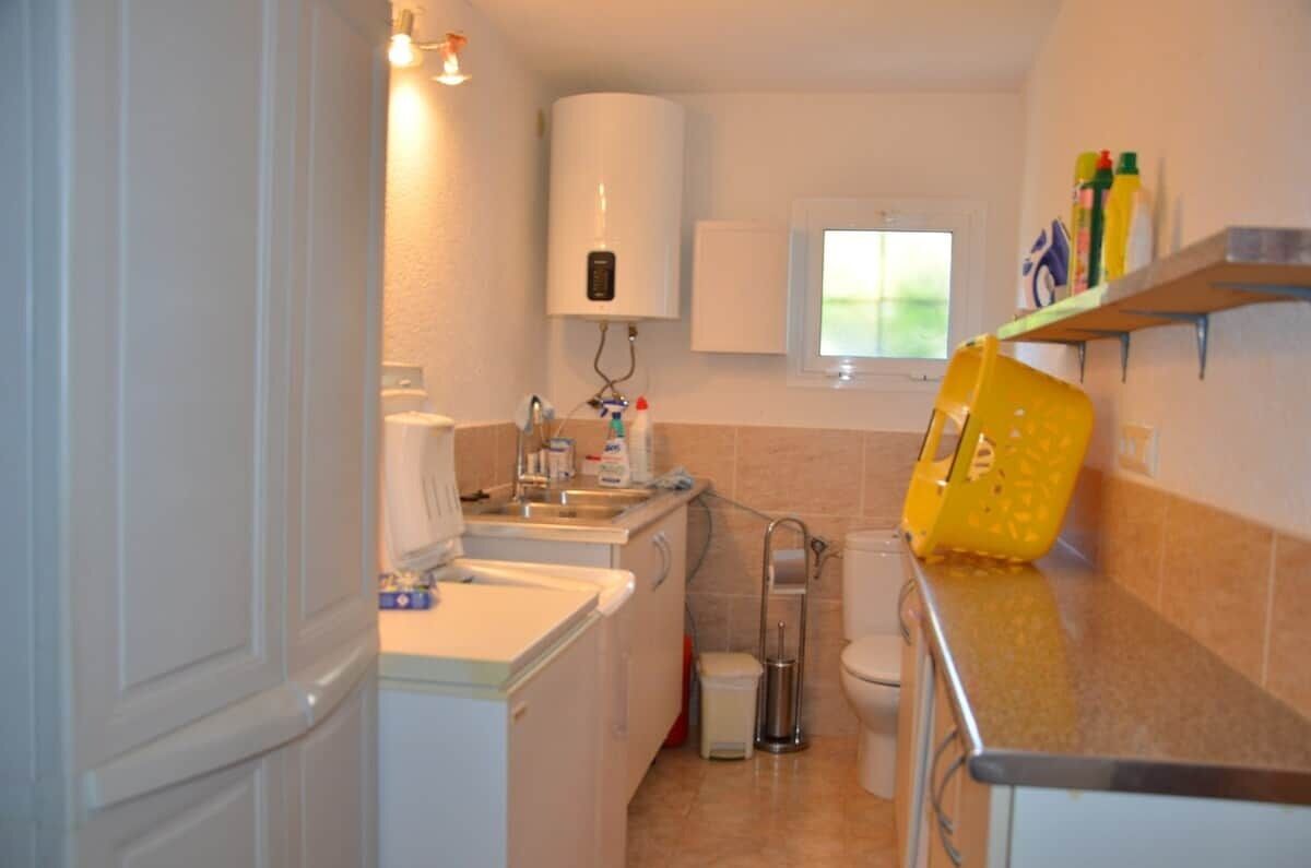 A compact kitchen with a sink, a white water heater, a toilet, and a window.