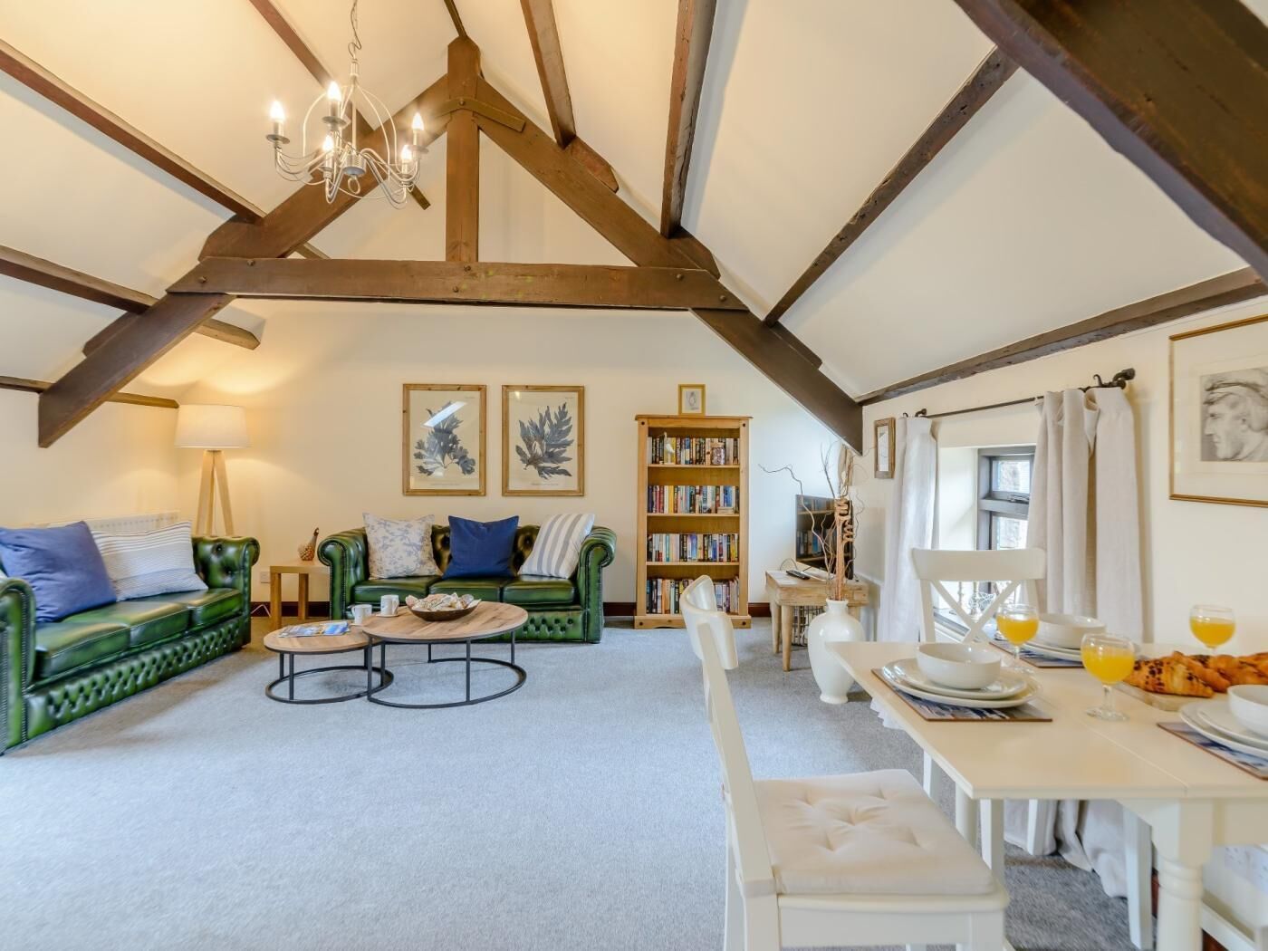 A cozy living room with a green sofa, a coffee table, a bookshelf, and a dining area with a table set for breakfast.