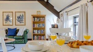 Una sala acogedora con un sofá verde, una estantería de madera y una mesa de comedor con cosas para el desayuno.