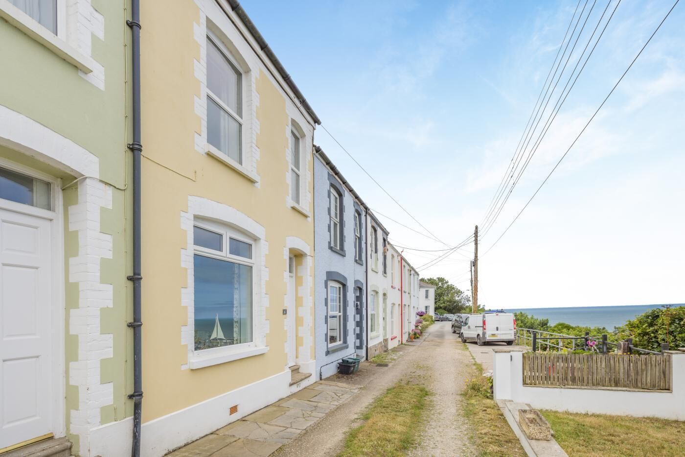 Une rue étroite bordée de maisons à étages, un fourgon blanc garé sur le côté et un ciel dégagé.